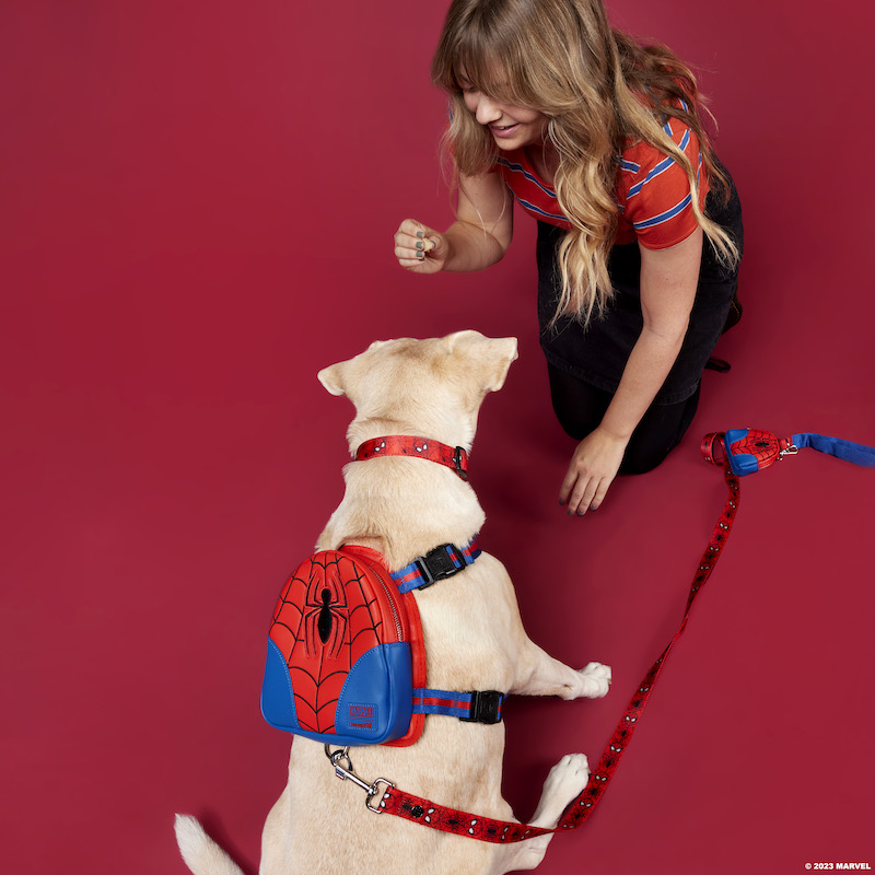 Woman and yellow lab sitting on the ground together against a red background. The dog wears the Spider-Man mini backpack harness, Spider-Man dog collar, and Spider-Man leash.